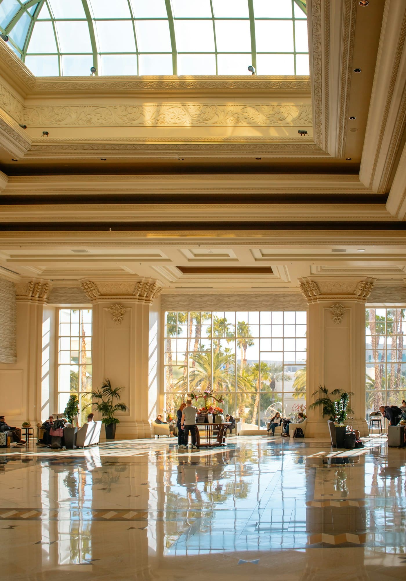 Grand luxury hotel lobby with palm trees visible through the windows