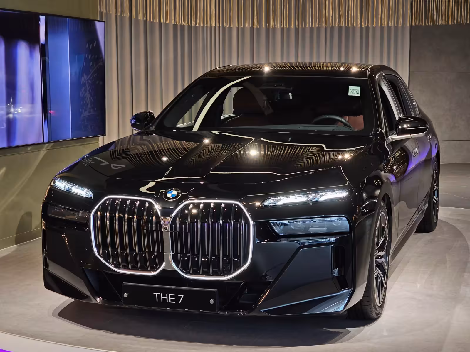 Black BMW luxury SUV in a showroom, front grille and sleek LED headlights prominent, 'THE 7' plate visible