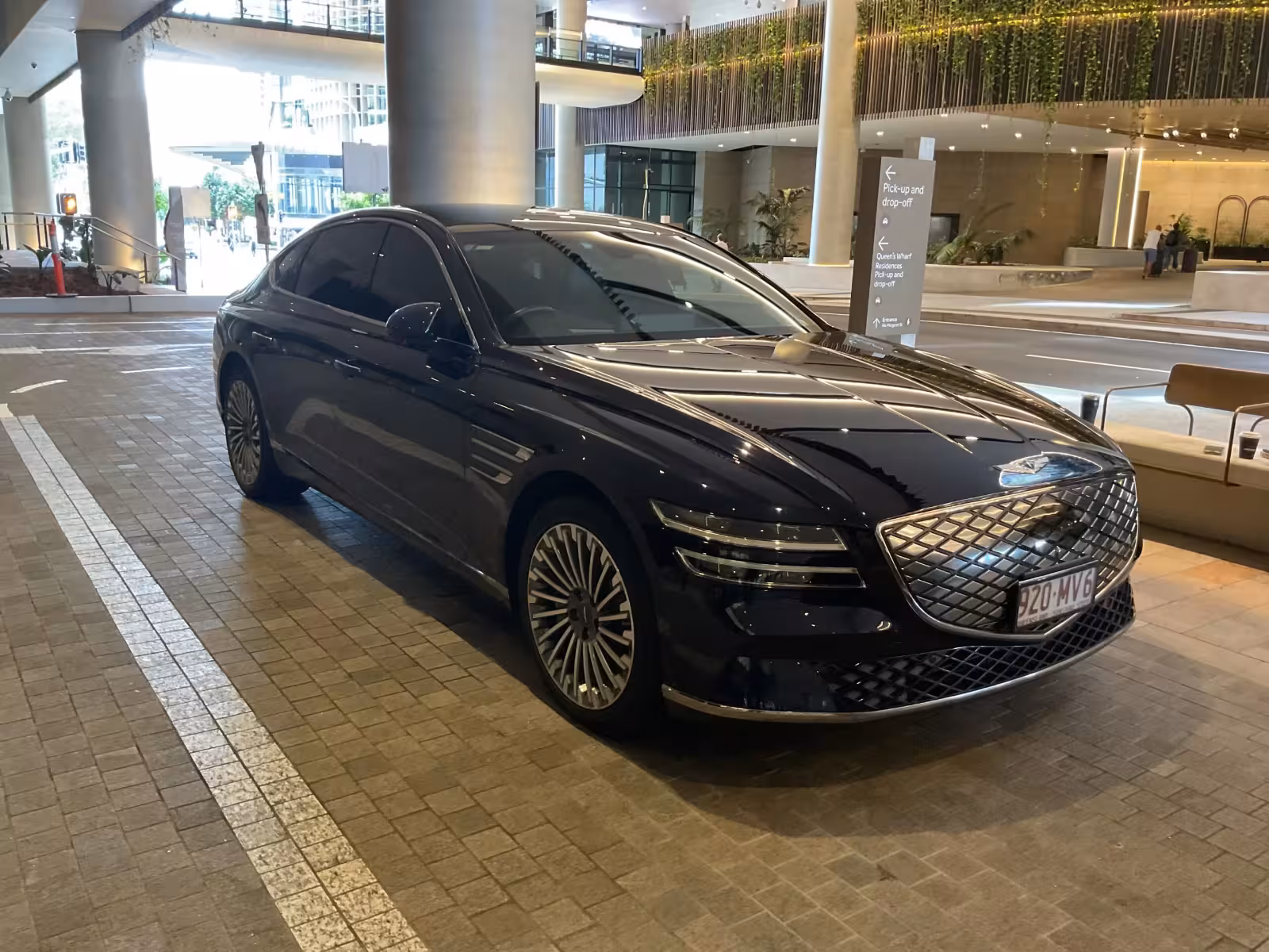 Black luxury sedan parked indoors at a hotel lobby drop-off area, glossy finish and distinctive front grille visible